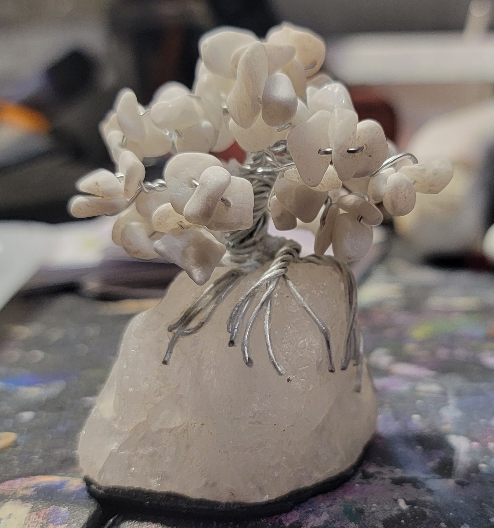 A handcrafted decorative tree made of white stones attached to a silver wire base, sitting on a natural stone pedestal.