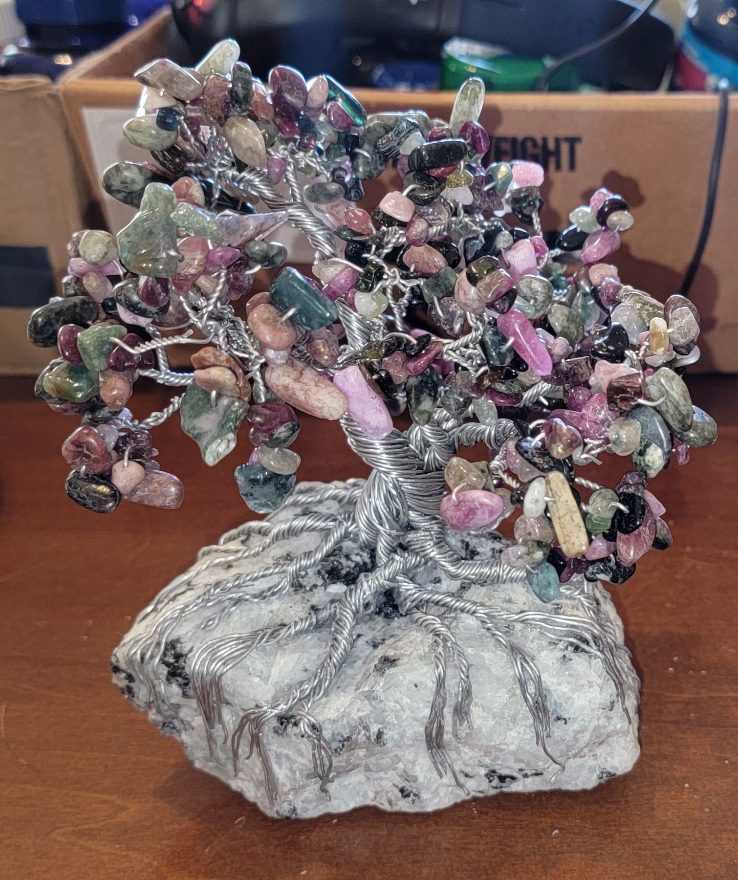 A decorative wire tree sculpture with colorful gemstone leaves, sitting on a stone base.