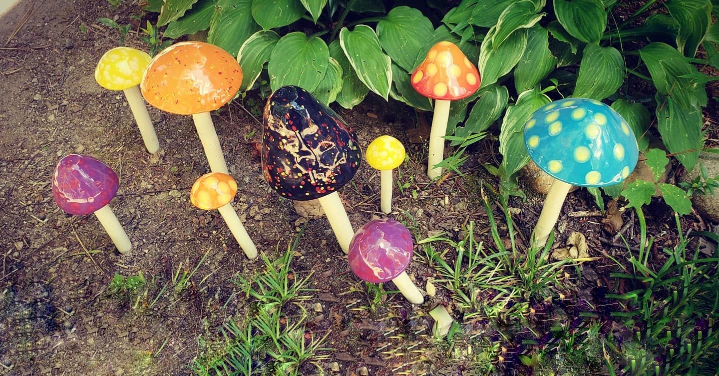 Colorful decorative mushrooms in various shapes and sizes placed in a garden setting, surrounded by green plants.